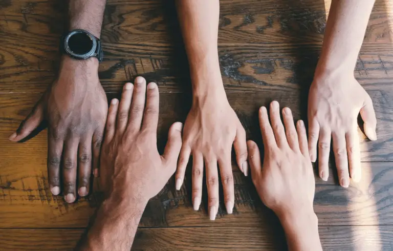 Hands of different ethnicities palm down on a wooden table