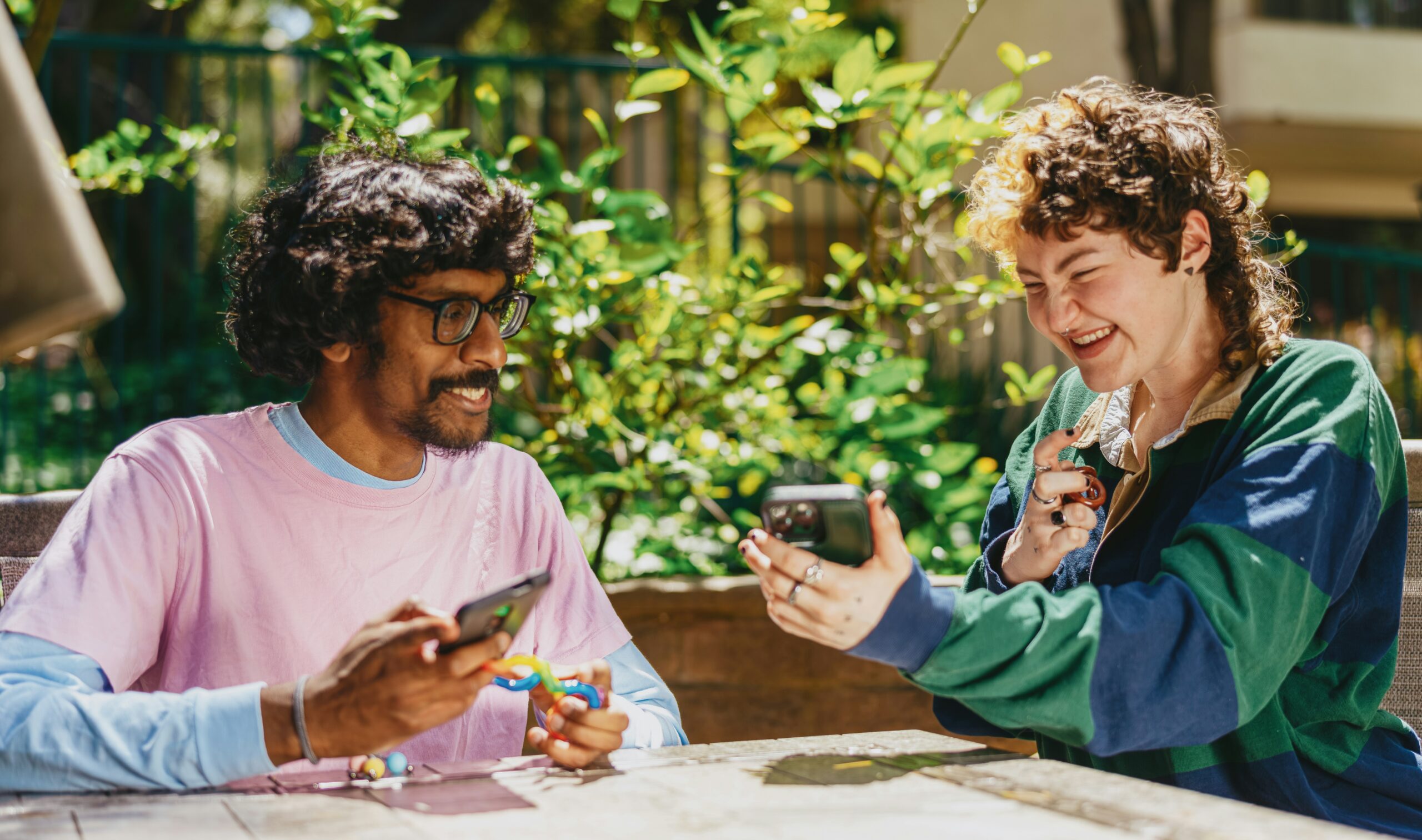 Two people sit outside in a garden sharing conversation about something on their phones